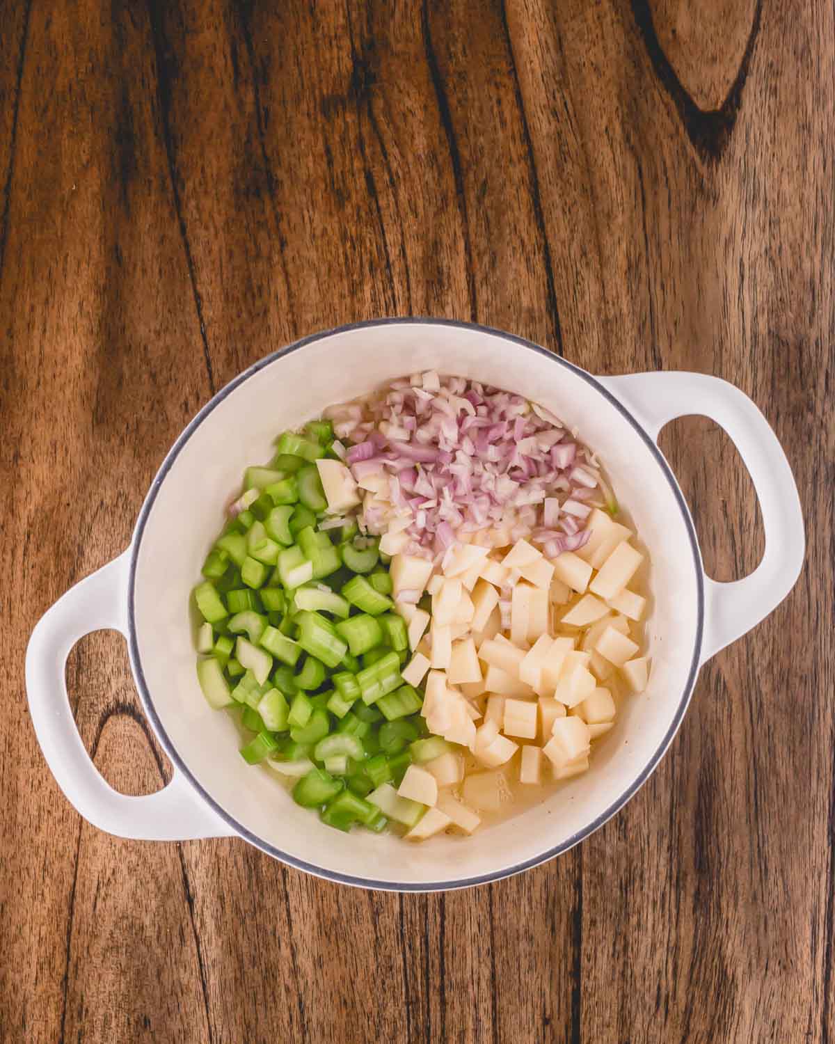 Shallots, potatoes, and celery being added to a pot of oyster stew.