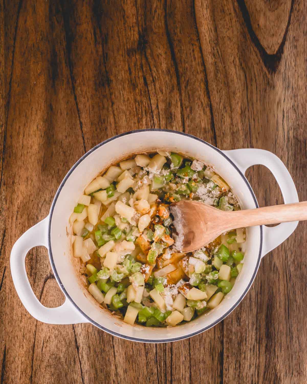 Potatoes, celery, and shallows being added to a pot of oyster stew.