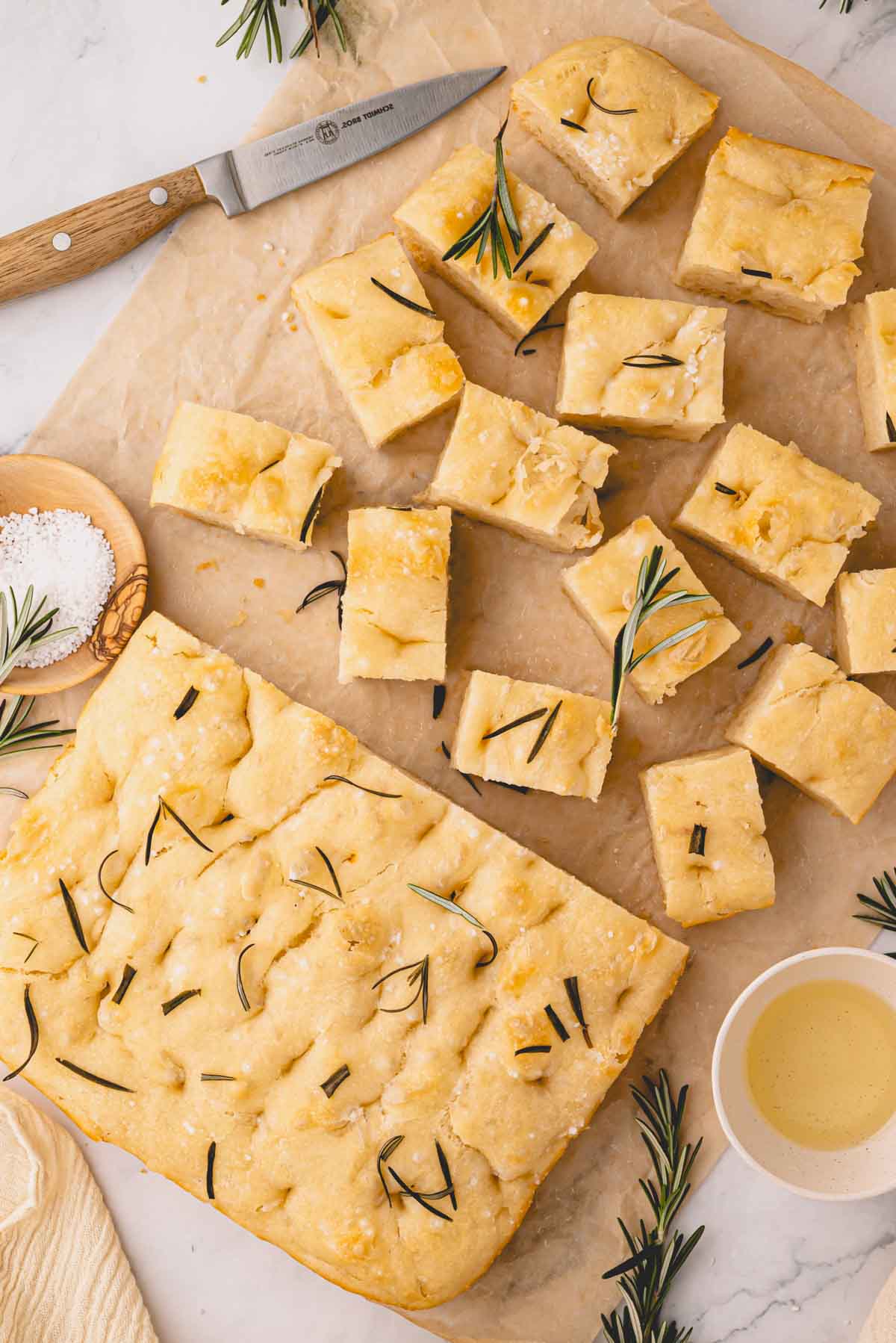 Half a loaf of rosemary focaccia bread and the rest of the bread sliced into squares on parchment paper.