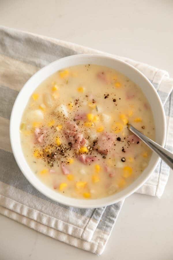 Overhead image of ham, potato and corn soup in a white bowl with a spoon and linen.