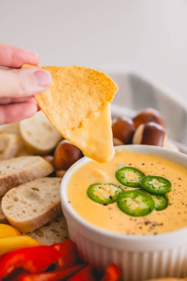 A hand dipping a chip into spicy cheddar dip.