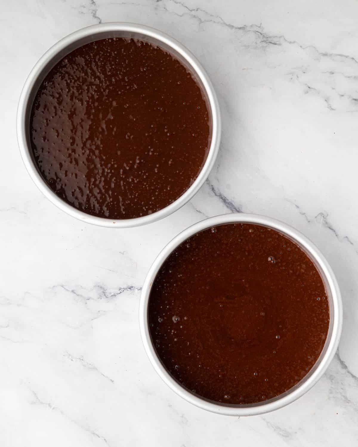 Two round cake pans with chocolate cake batter.