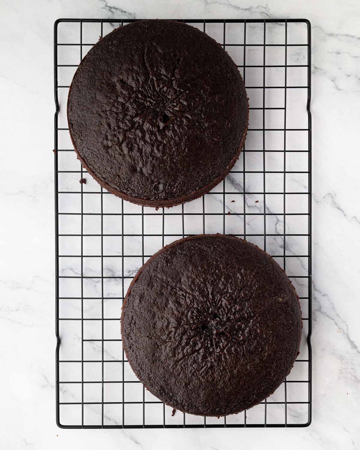 Two round chocolate cakes on a wire rack.
