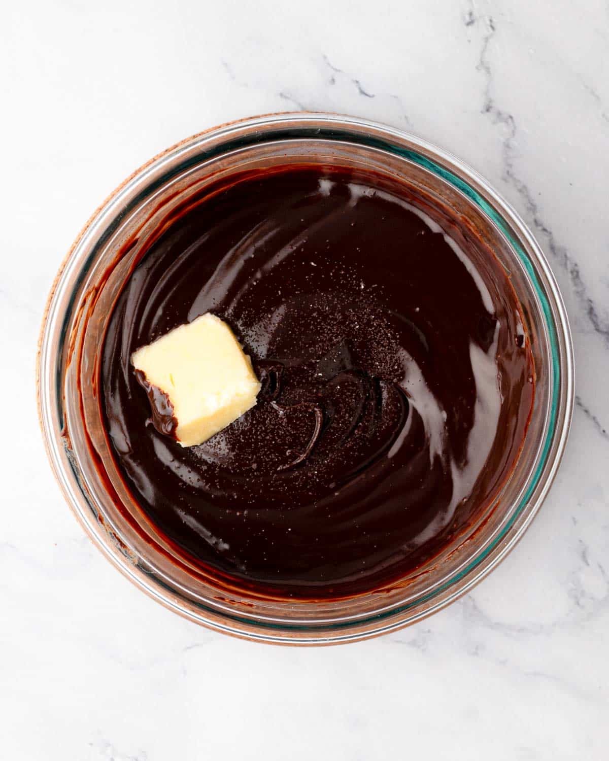 A knob of butter in a bowl of chocolate Swiss meringue buttercream frosting.