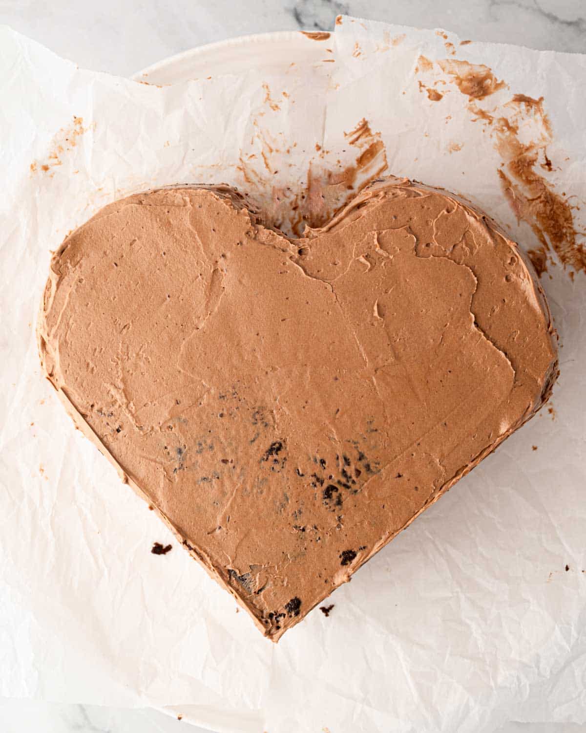 A chocolate heart cake being frosted with chocolate Swiss meringue buttercream.