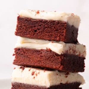 A stack of three red velvet brownies with cream cheese frosting on a plate.