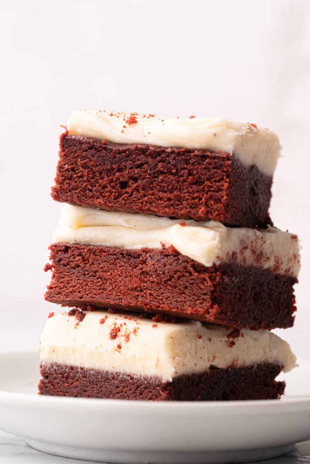 A stack of three red velvet brownies with cream cheese frosting on a plate.