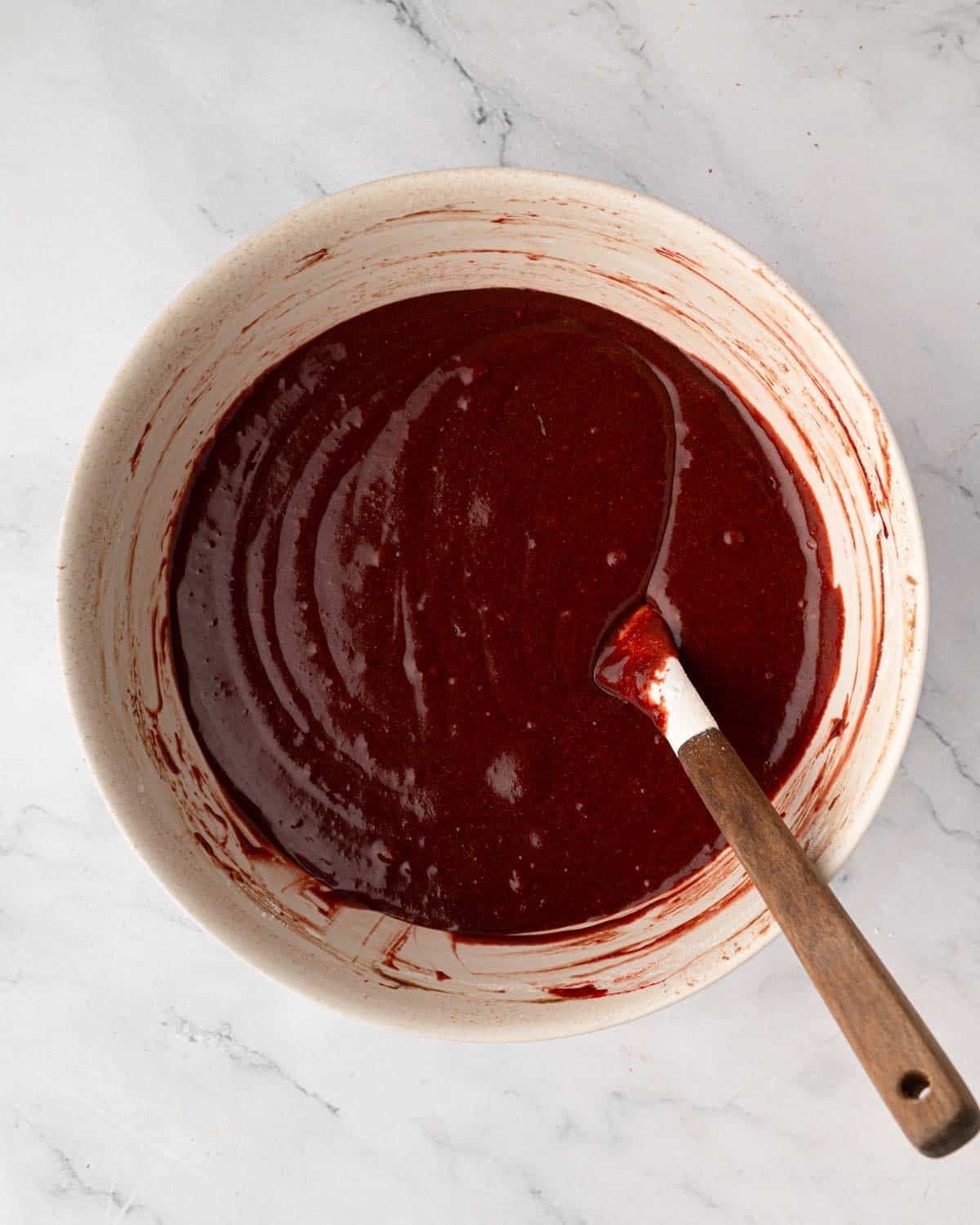A bowl of red velvet brownie batter with a rubber spatula sticking out.