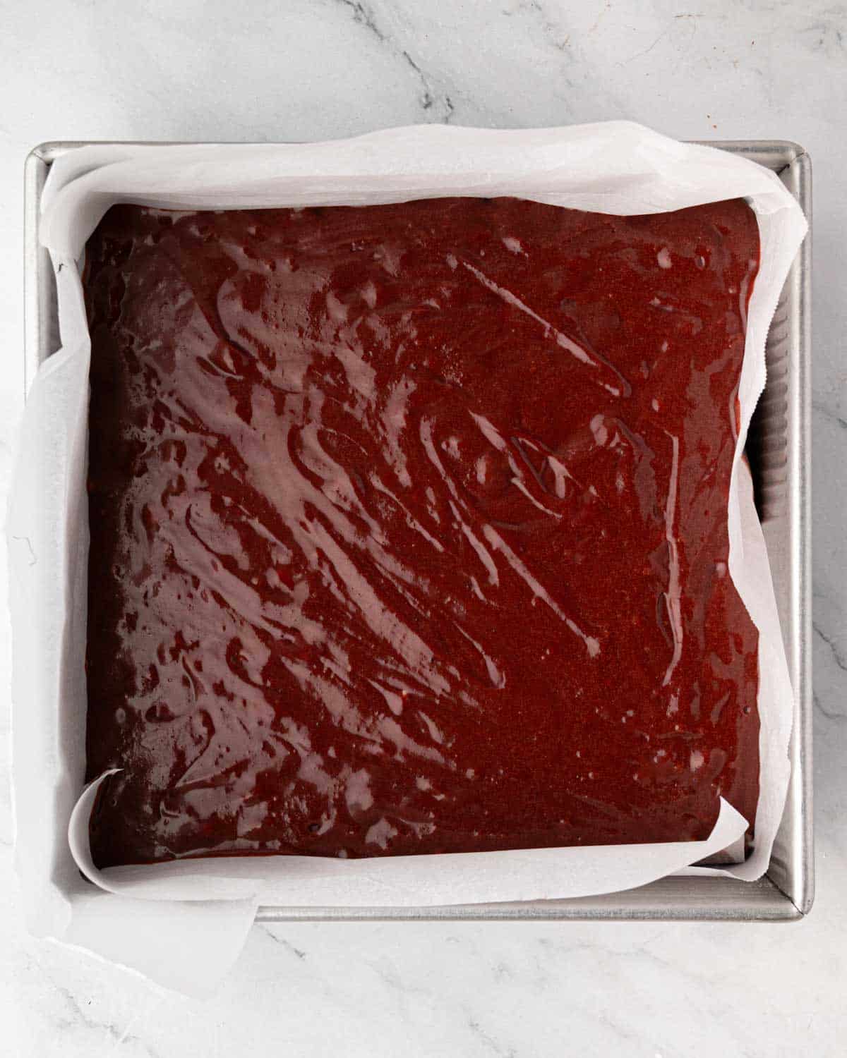 Uncooked red velvet brownie batter in a square baking pan lined with parchment paper.