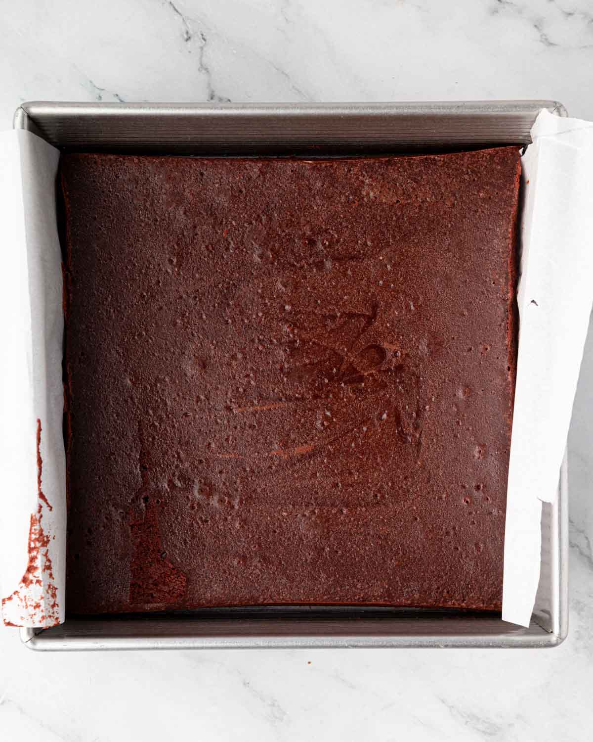 Baked red velvet brownies in a square baking pan lined with parchment paper.
