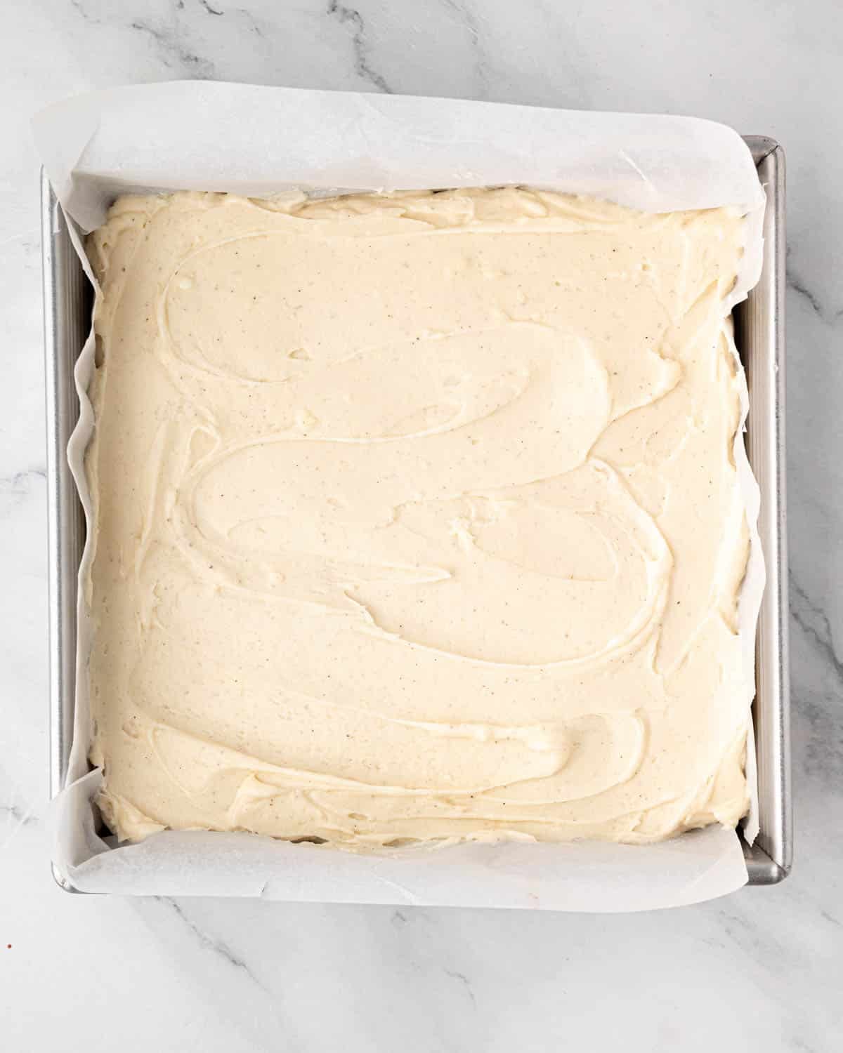 A square cake pan of red velvet brownies topped with cream cheese frosting.