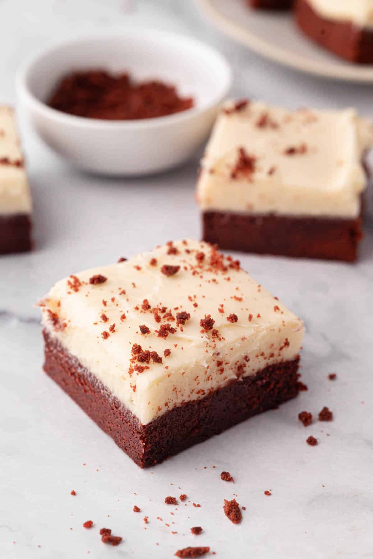 Two red velvet brownies topped with cream cheese frosting.