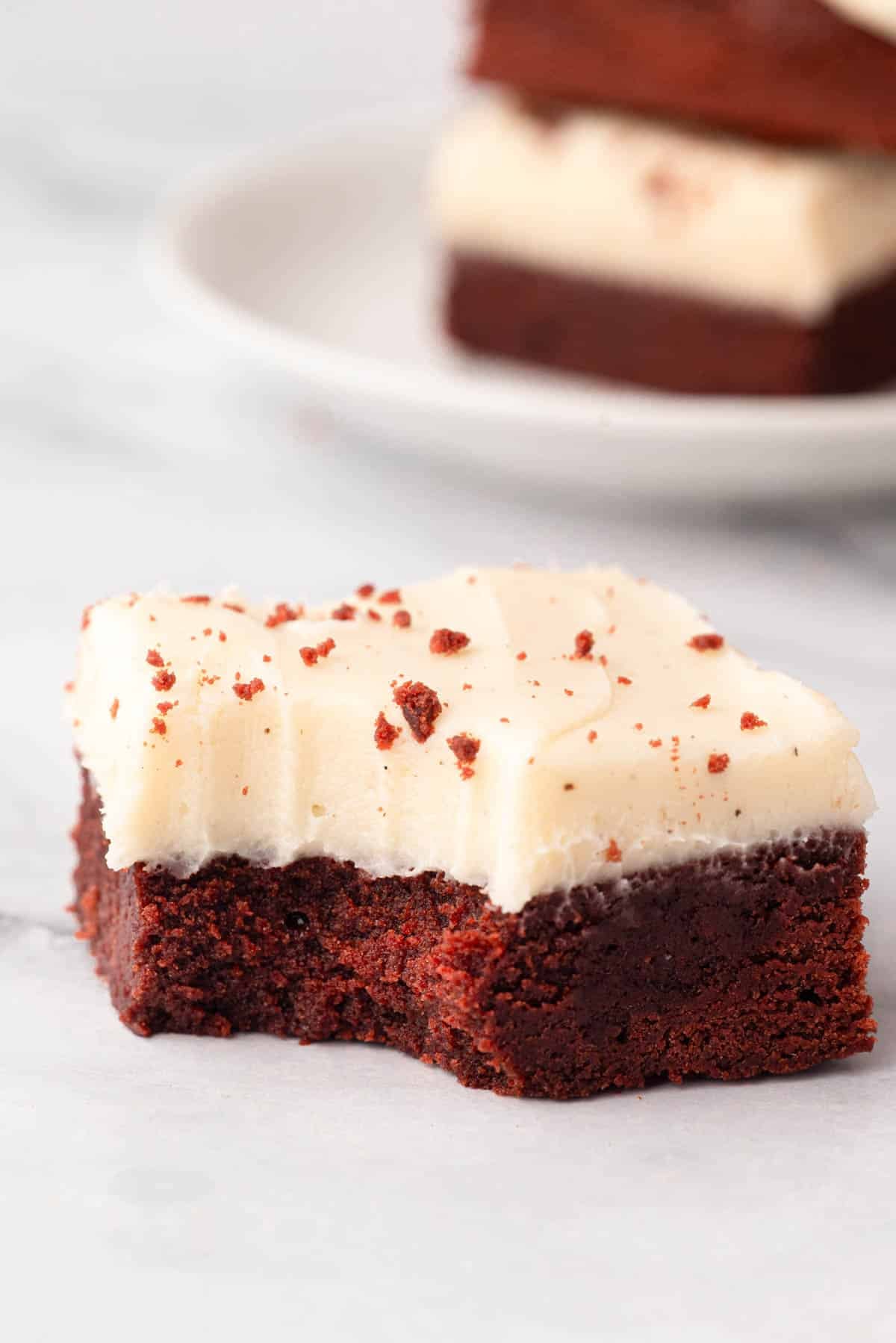 A red velvet cake brownie with cream cheese frosting missing a bite.