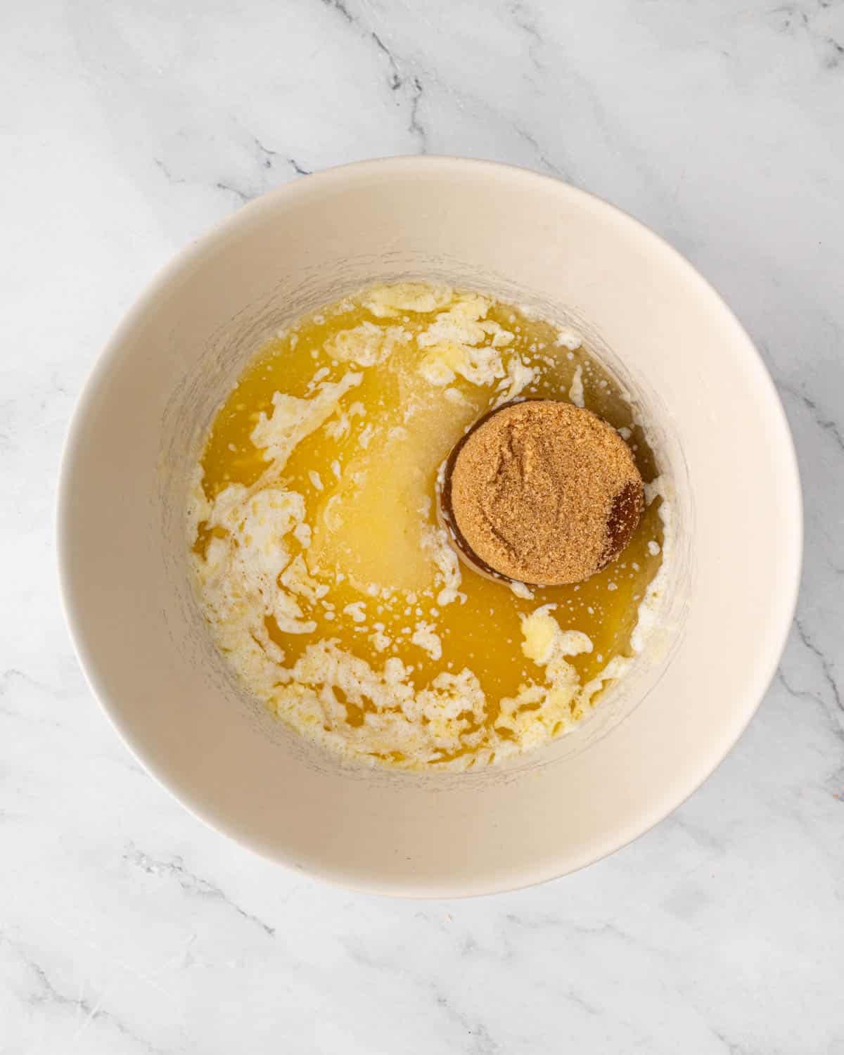 Sugar being added to a bowl of wet ingredients for red velvet brownies.