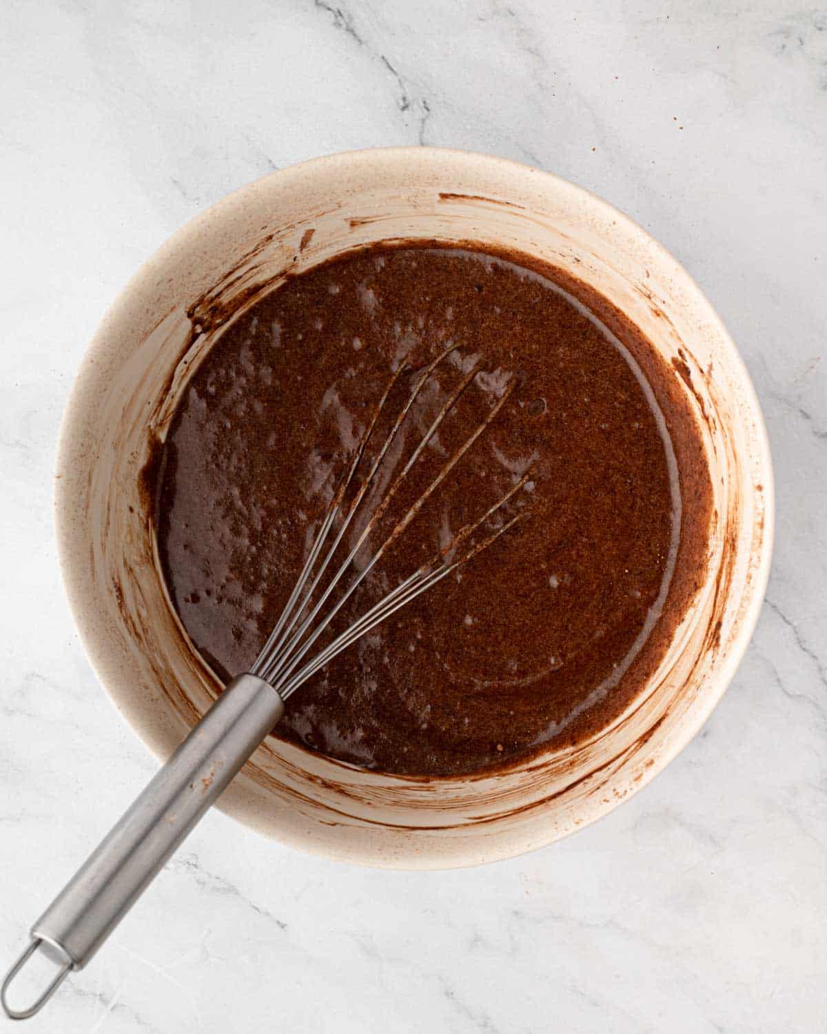 Red velvet brownie batter in a bowl with a whisk sticking out.