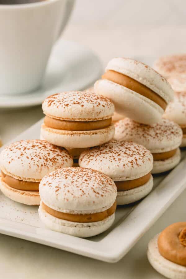 Tiramisu macarons stacked on a long white serving plate.