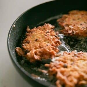 A cast iron skillet with cooking cheesy potato pancakes.
