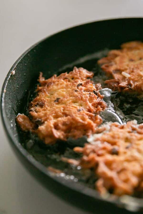 A cast iron skillet with cooking cheesy potato pancakes.