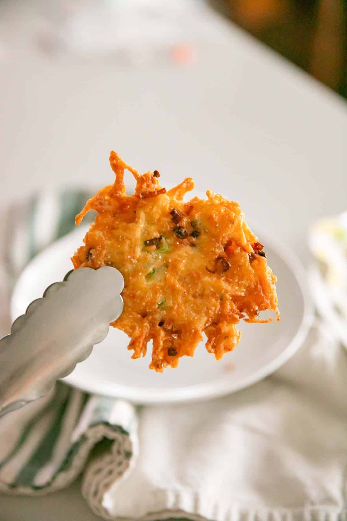 A cheesy potato pancake being held by tongs with a white plate in the background.