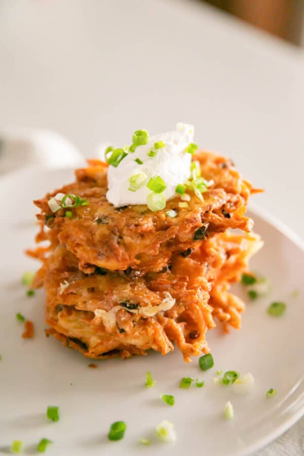 Cheesy potato pancakes stacked with sour cream on top.