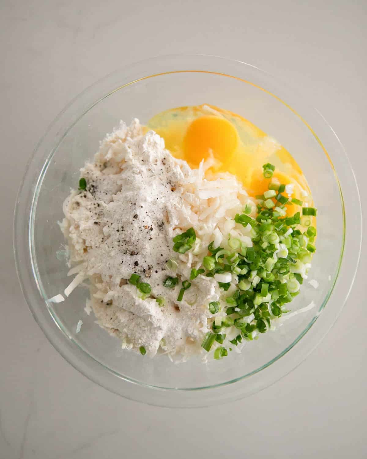 A glass bowl with ingredients for cheesy potato pancakes.