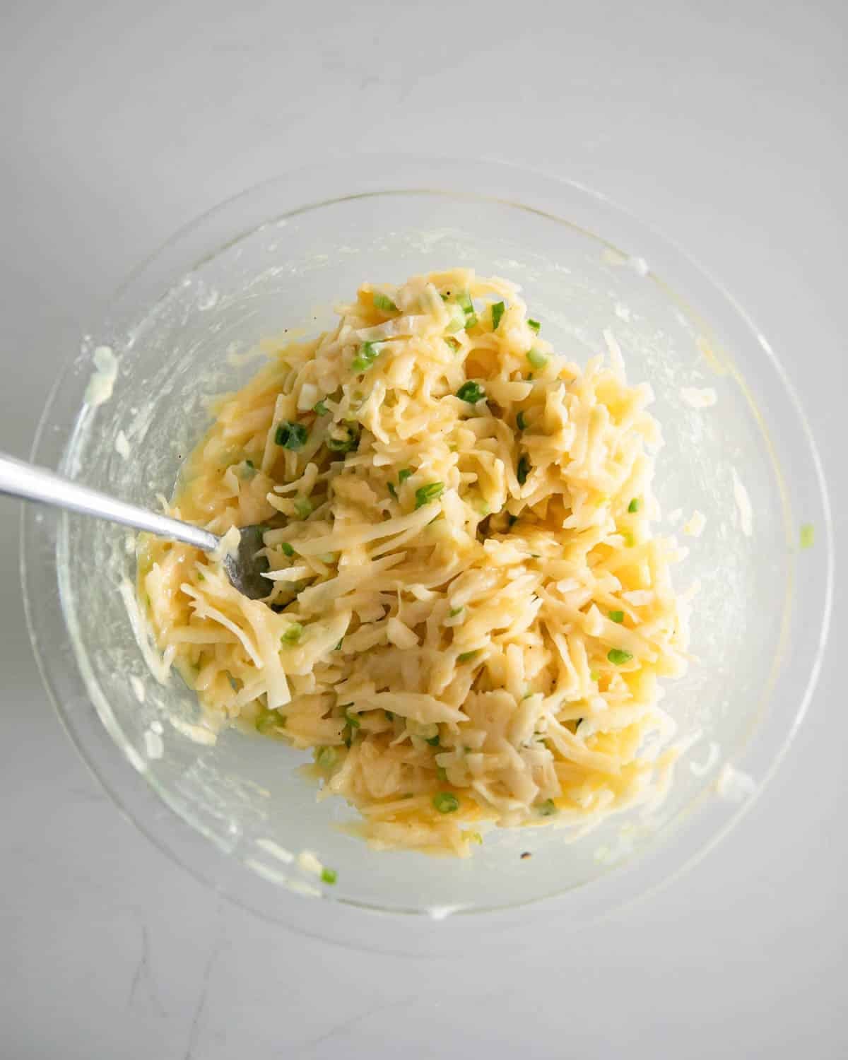A glass bowl with ingredients mixed for cheesy potato pancakes.