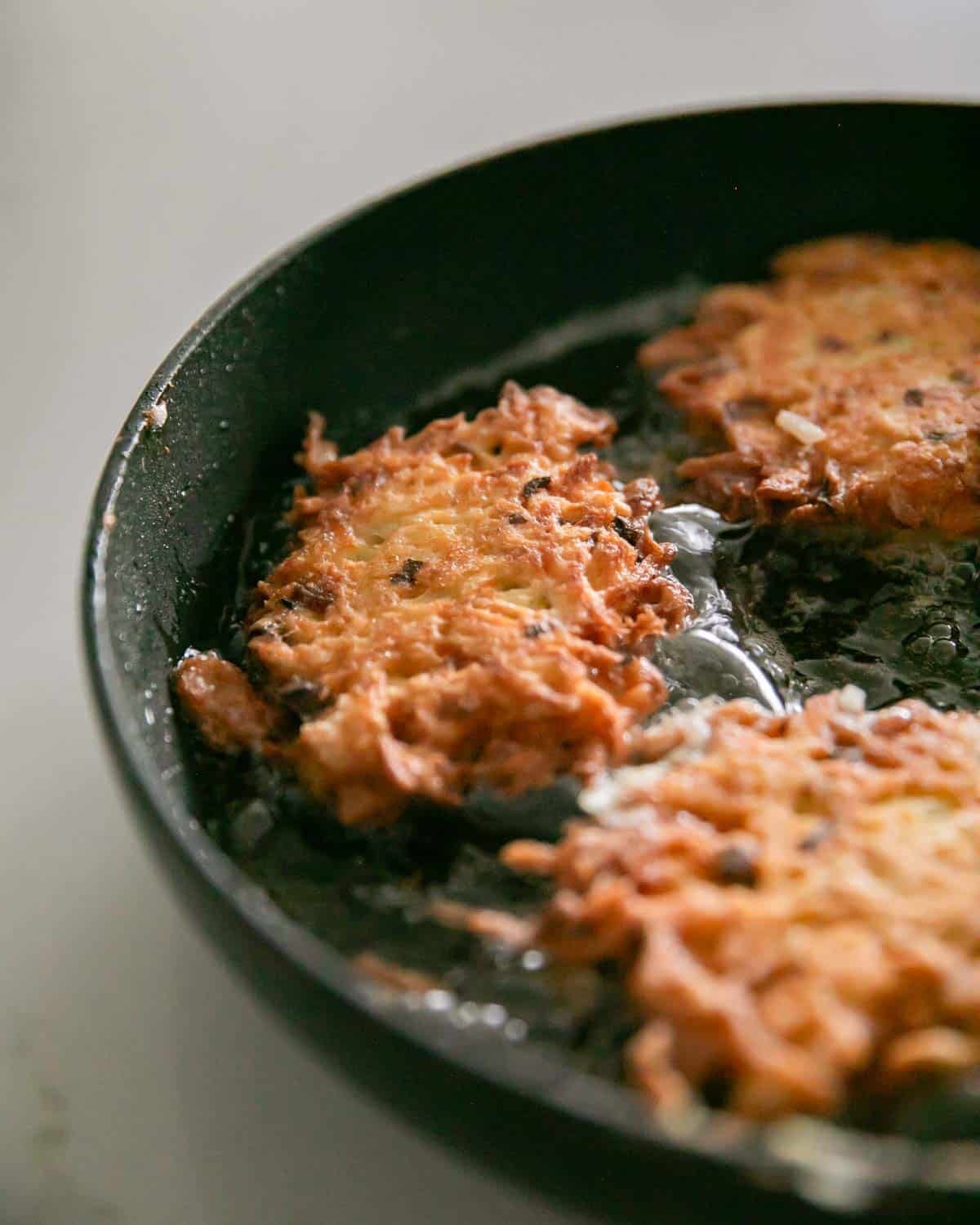 Cheesy potato pancakes flipped in a large cast iron skillet.