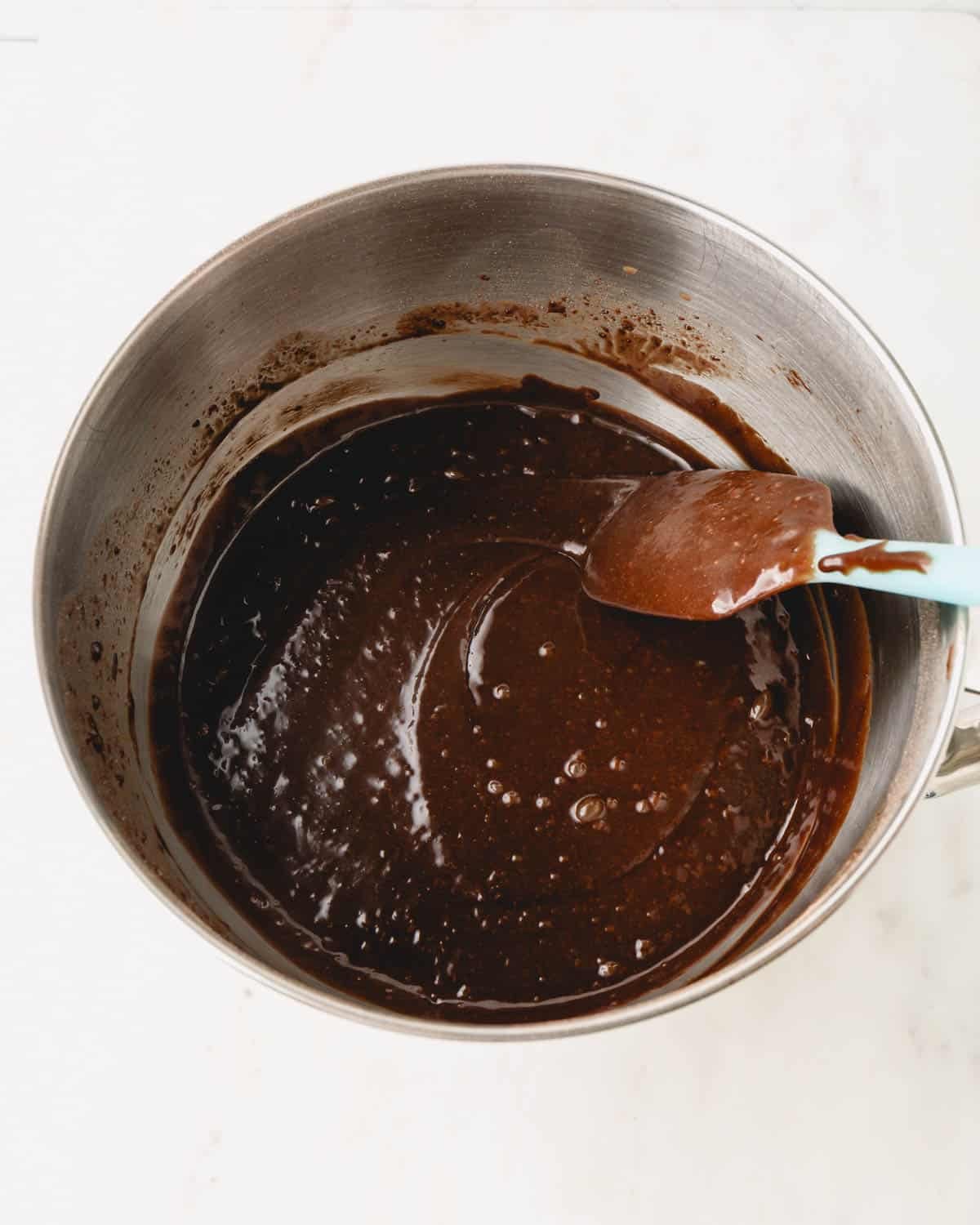 A metal mixing bowl with German chocolate cake batter and a spatula resting on the side.