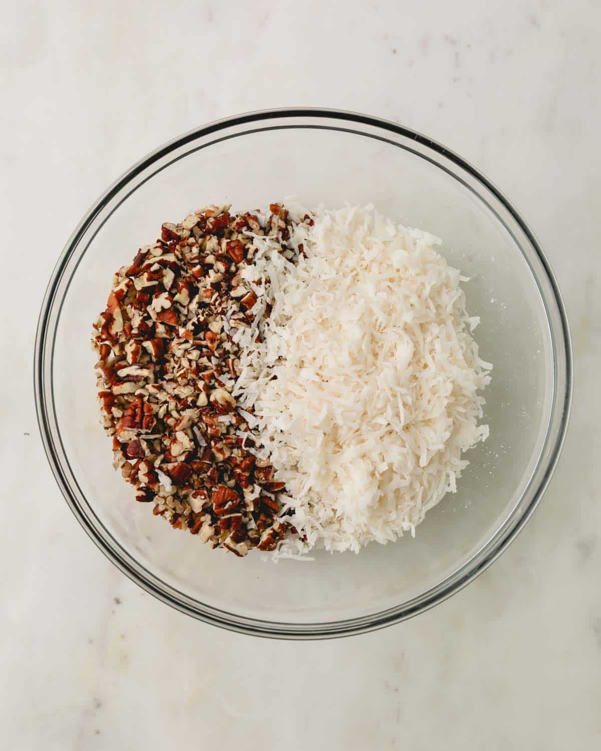 A glass bowl with pecans and coconut.