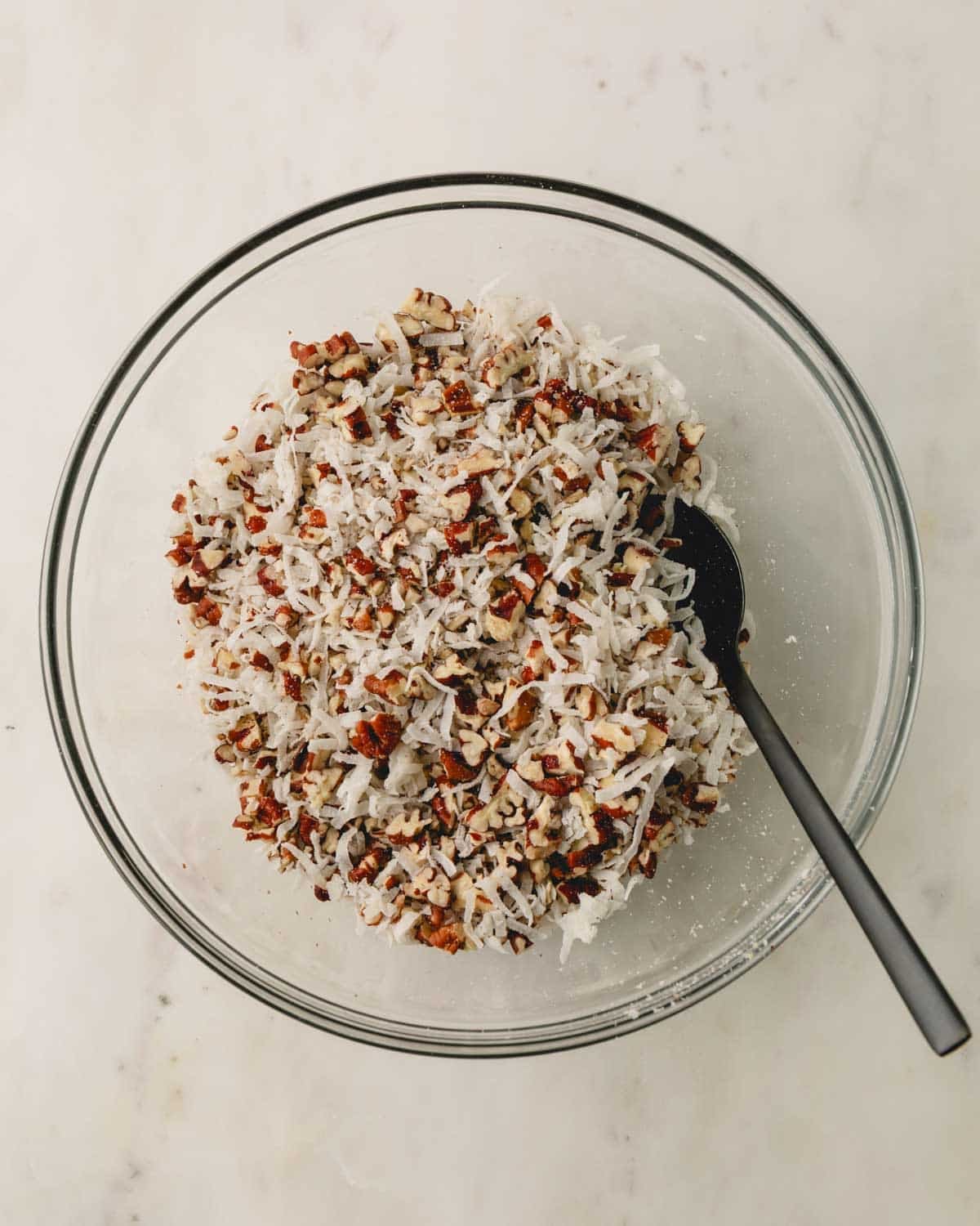 A glass bowl with pecans and coconut mixed.