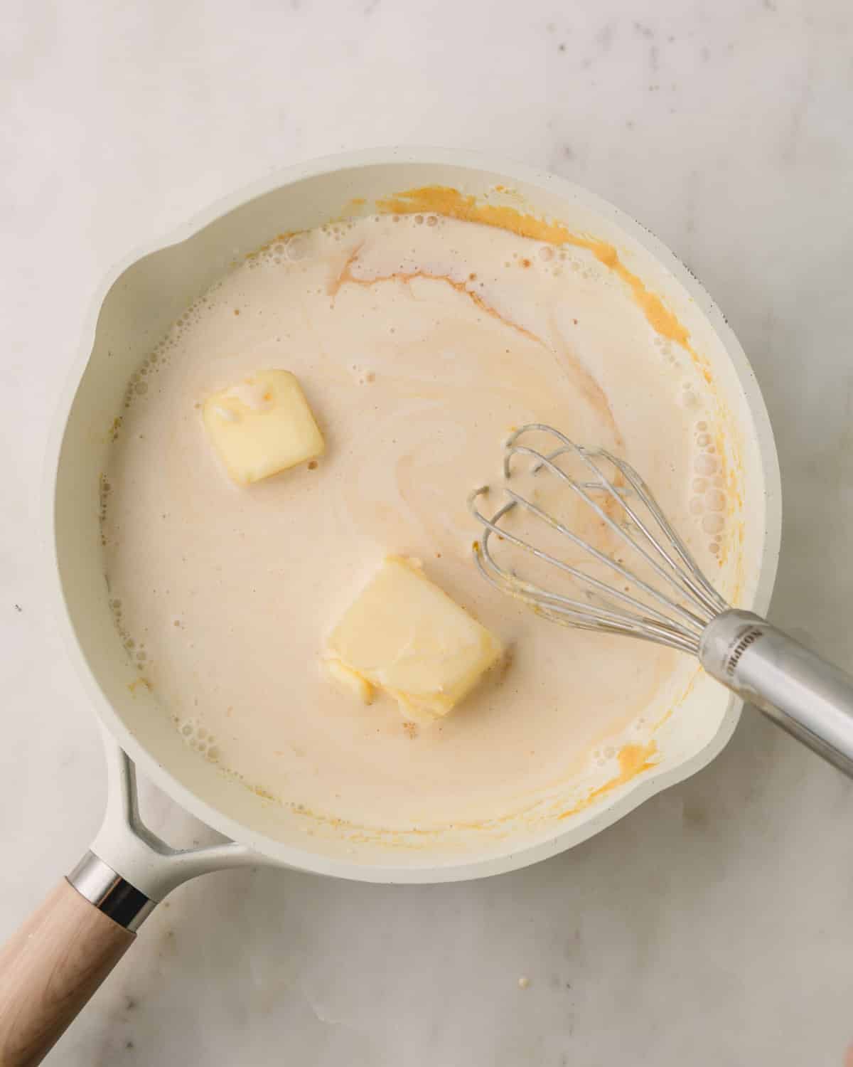 A pan with sugar, evaporated milk, and butter cooking with a whisk resting on the side.