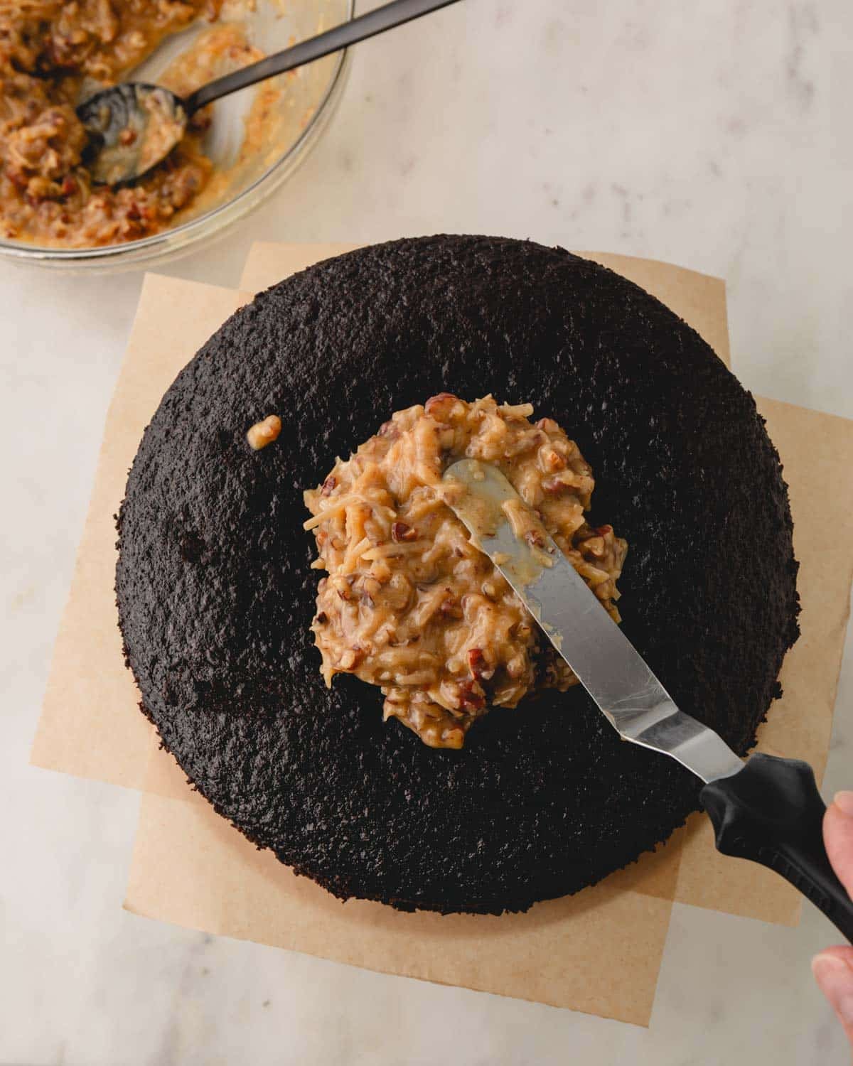 A German chocolate cake with coconut pecan frosting being spread.
