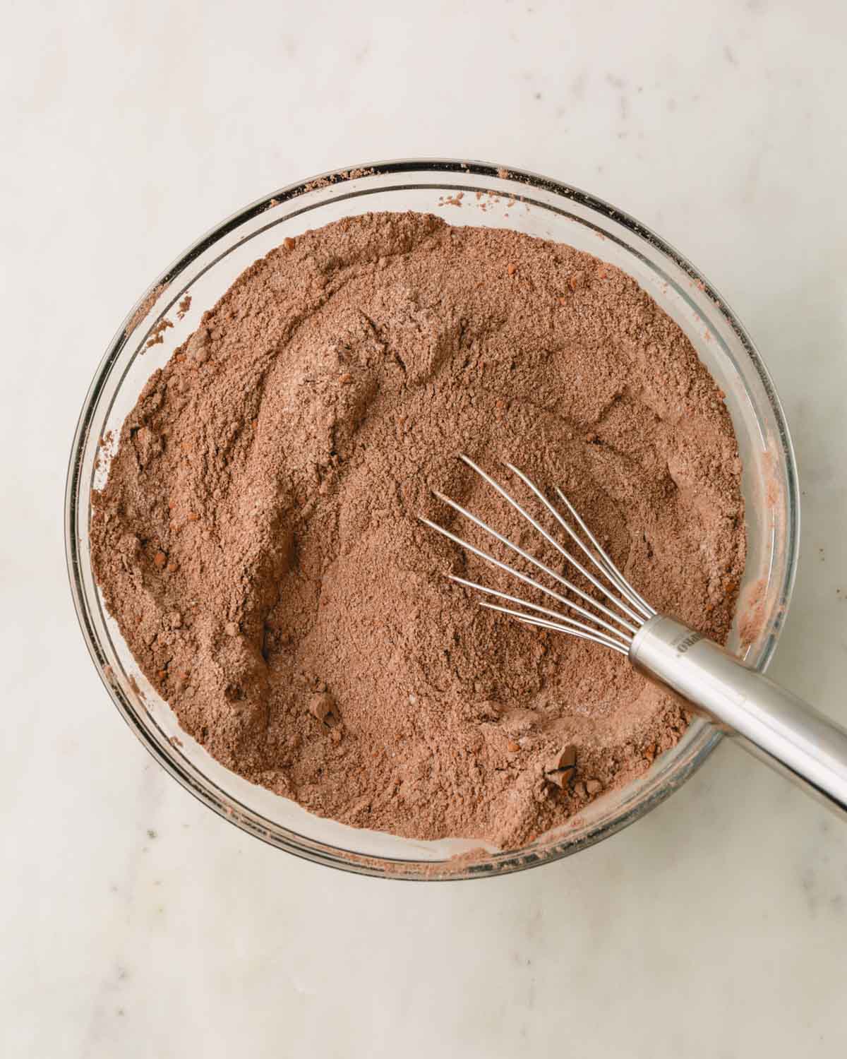 A glass bowl with the dry ingredients whisked together for German chocolate cake.