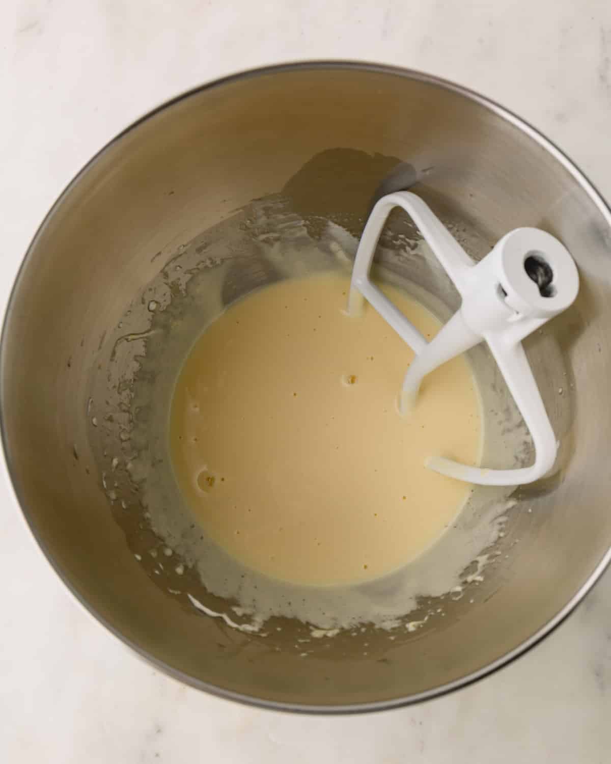 A metal bowl with wet ingredients mixed for German chocolate cake and a paddle attachment resting in the bowl.