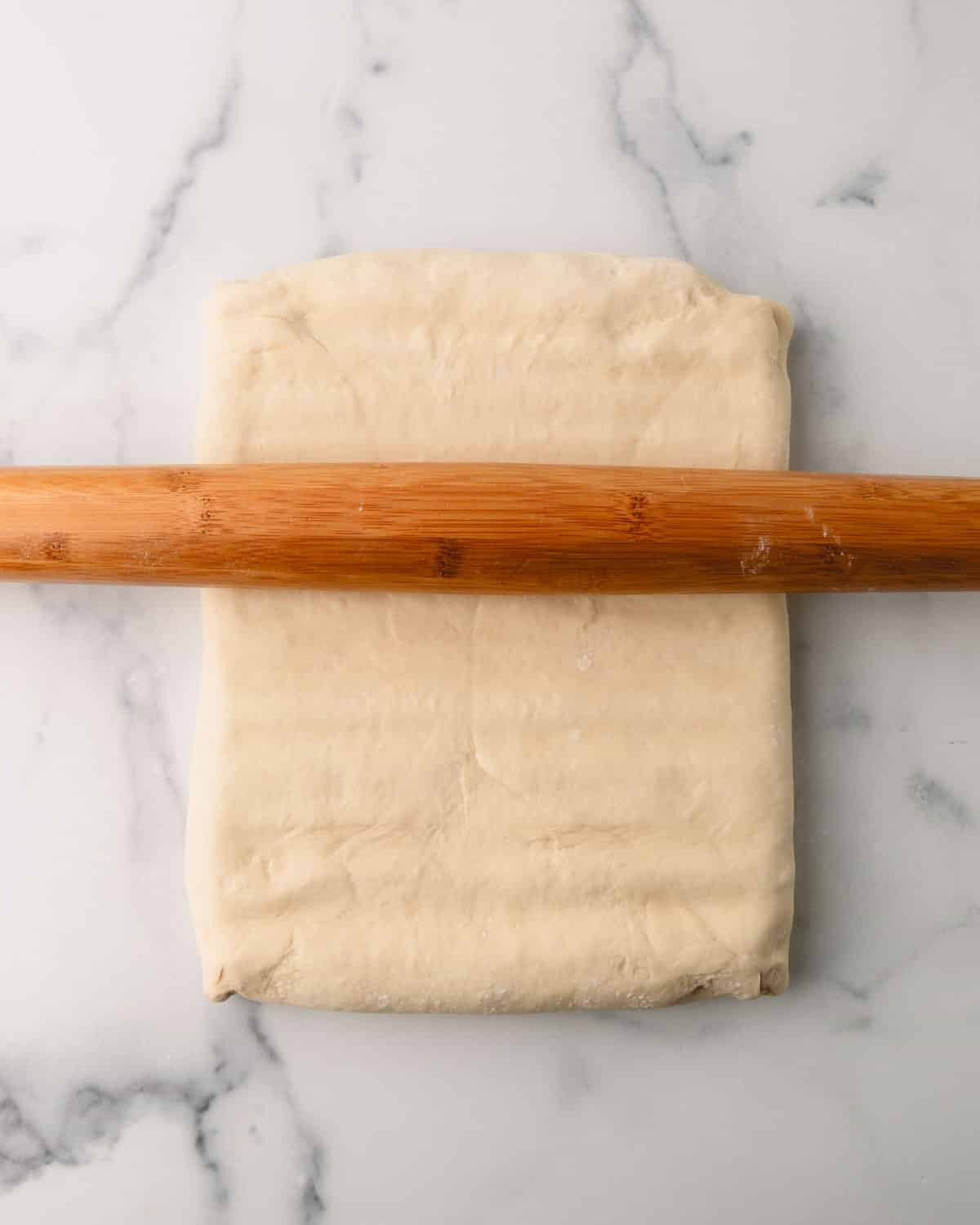 A rolling pin rolling out the butter and dough.