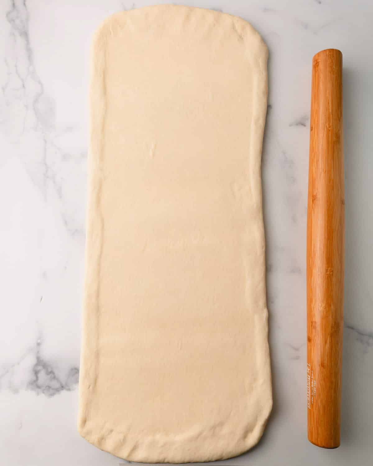 Rolling pin rolling out croissant dough into a rectangle.