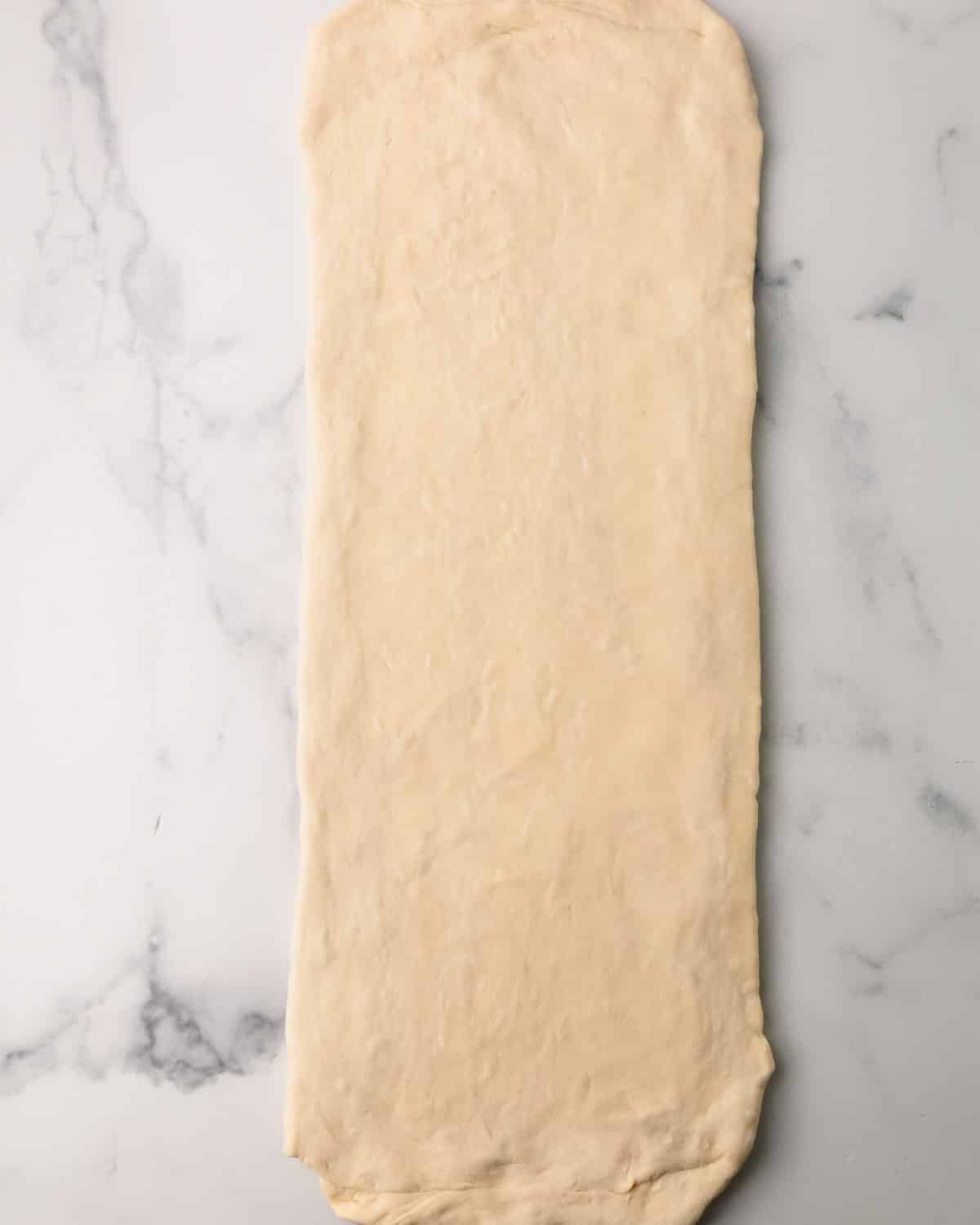 Croissant dough being rolled into a rectangle.