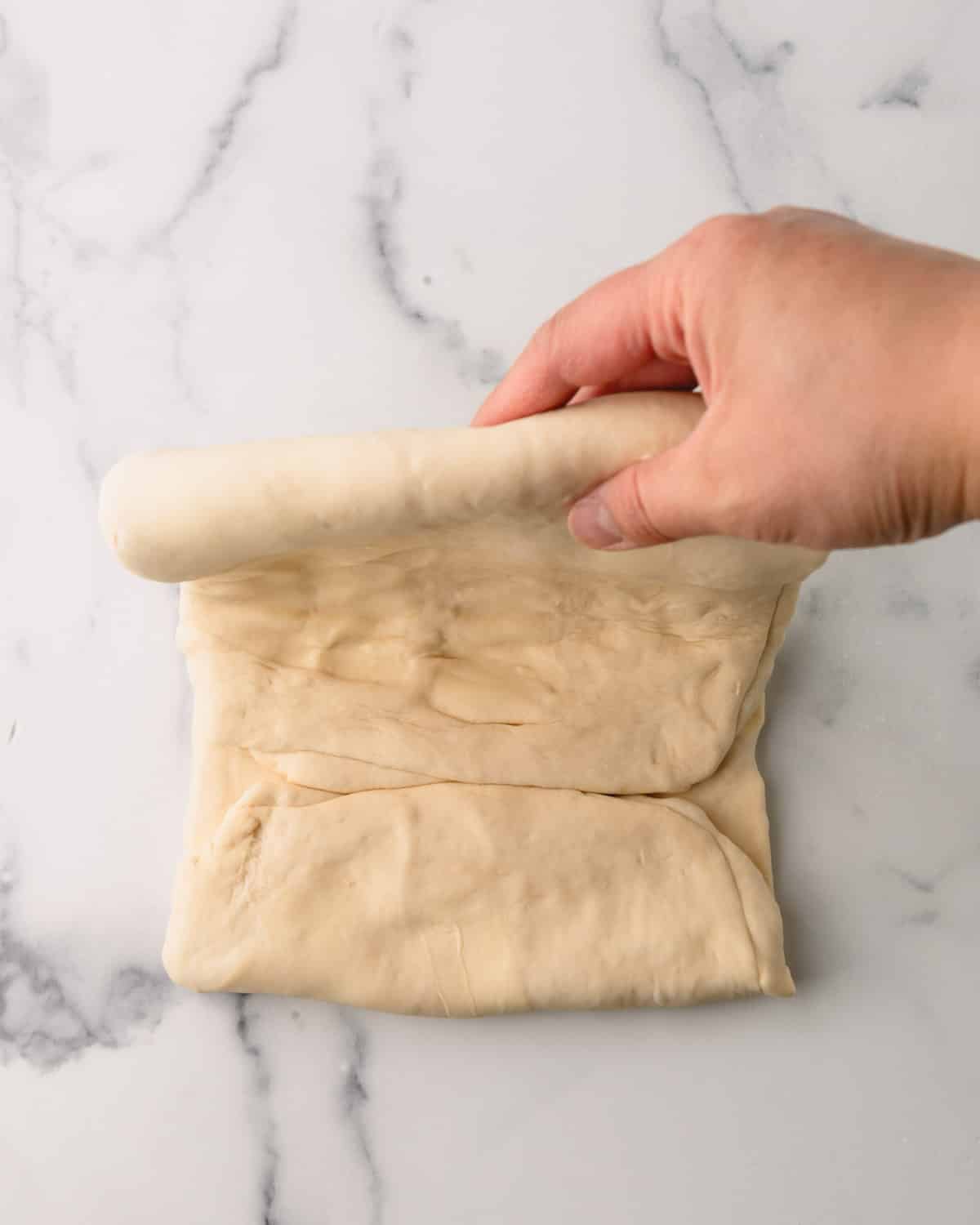 A hand folding croissant dough.
