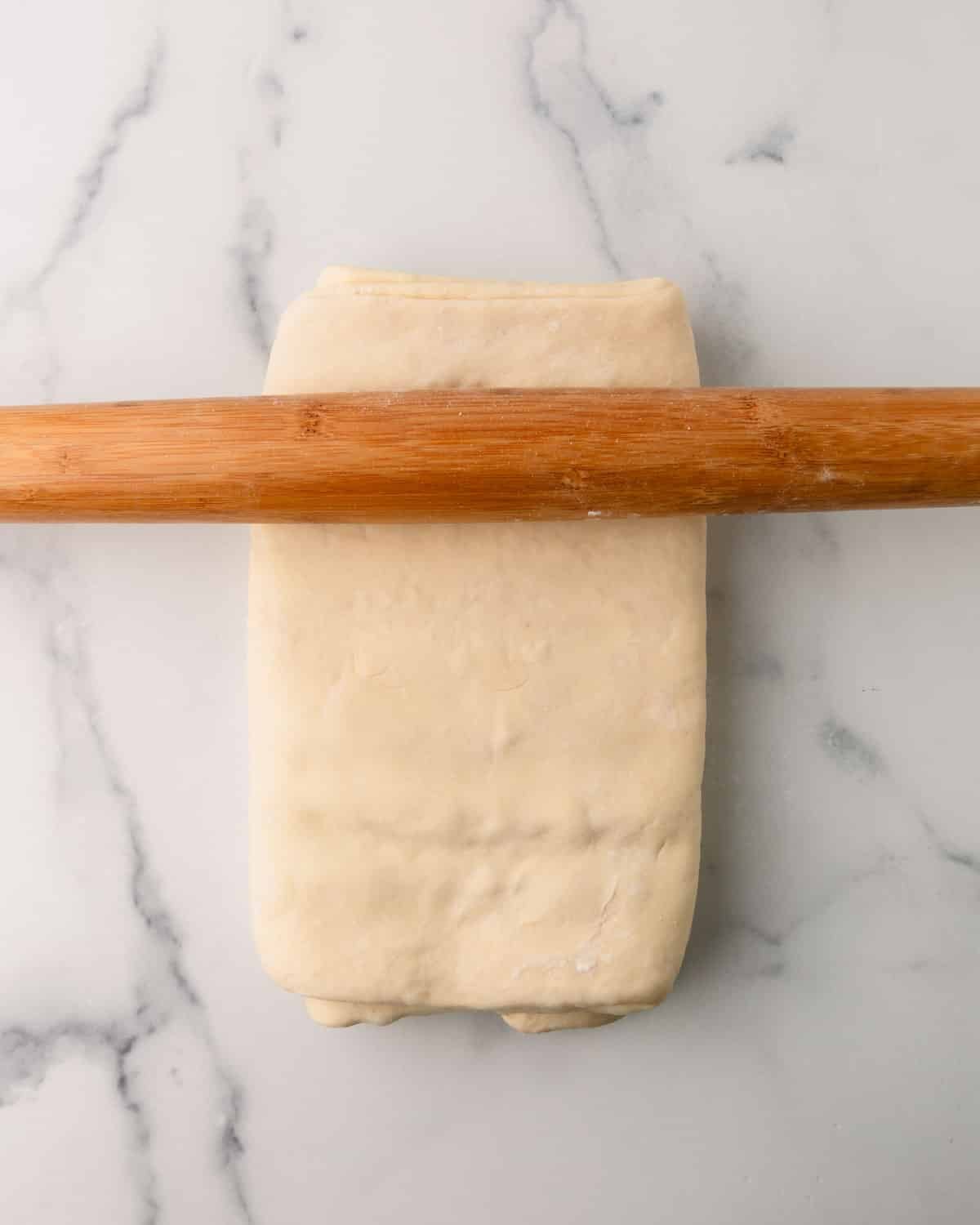 A rolling pin rolling out croissant dough.