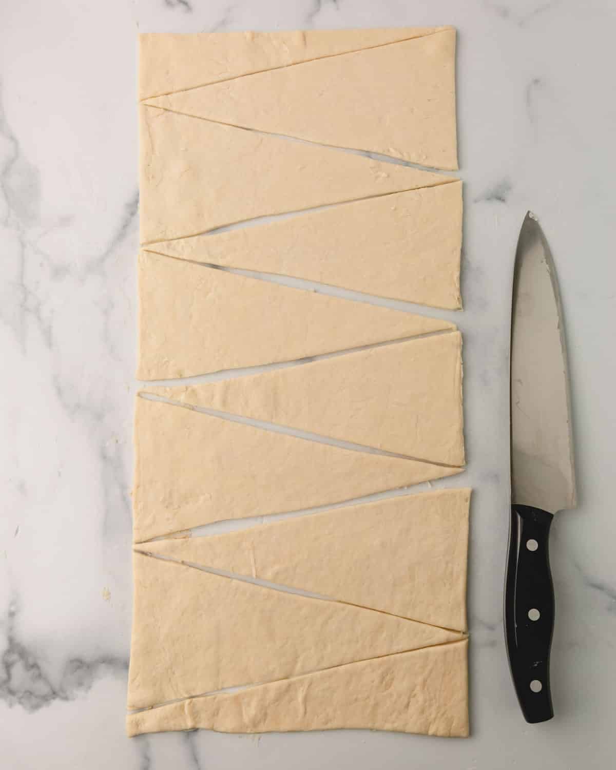 Croissant dough being cut into triangles.