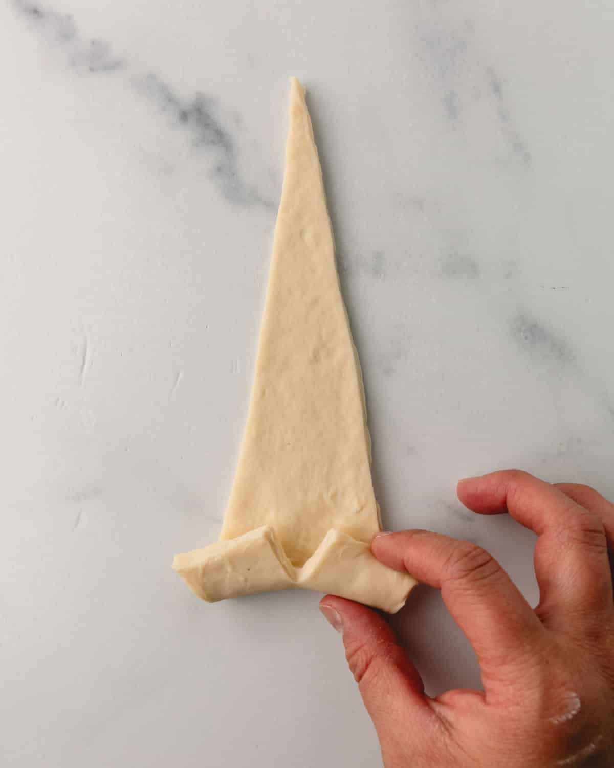 A hand rolling the croissant dough.
