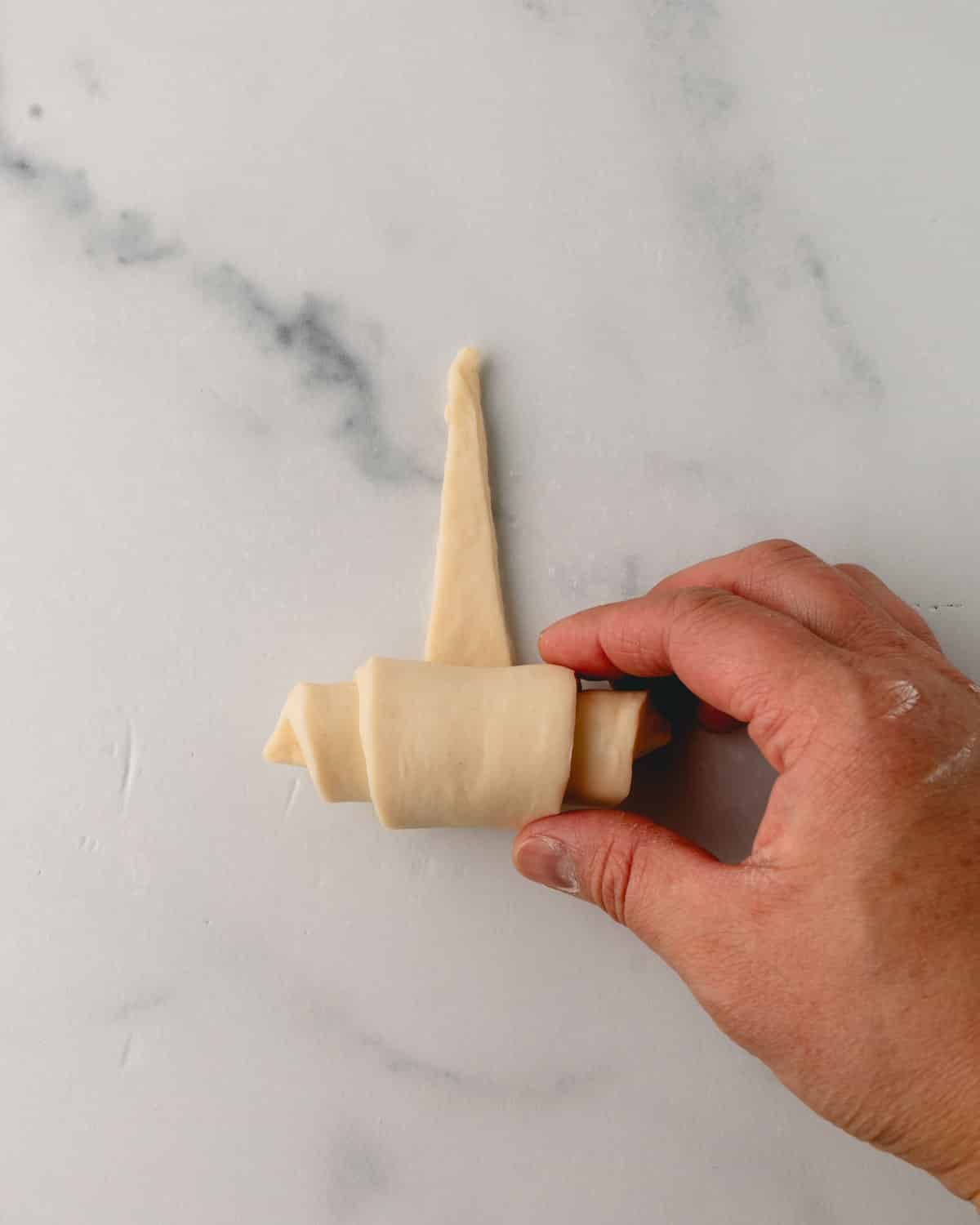 A hand rolling the croissant dough further.