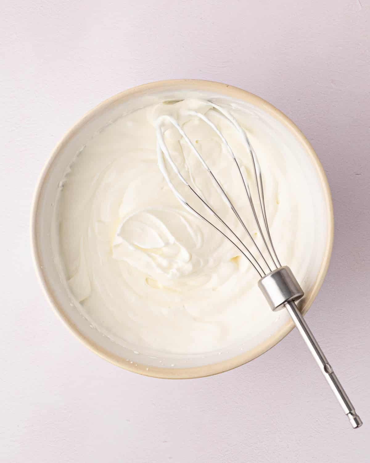 Whipped cream in a white bowl with a beater resting on the side.