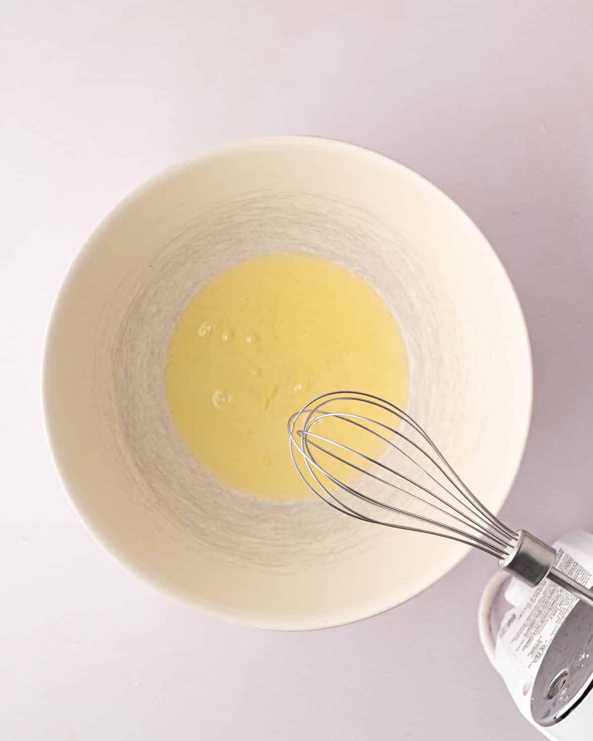 A hand mixer beater over a white bowl with egg whites.