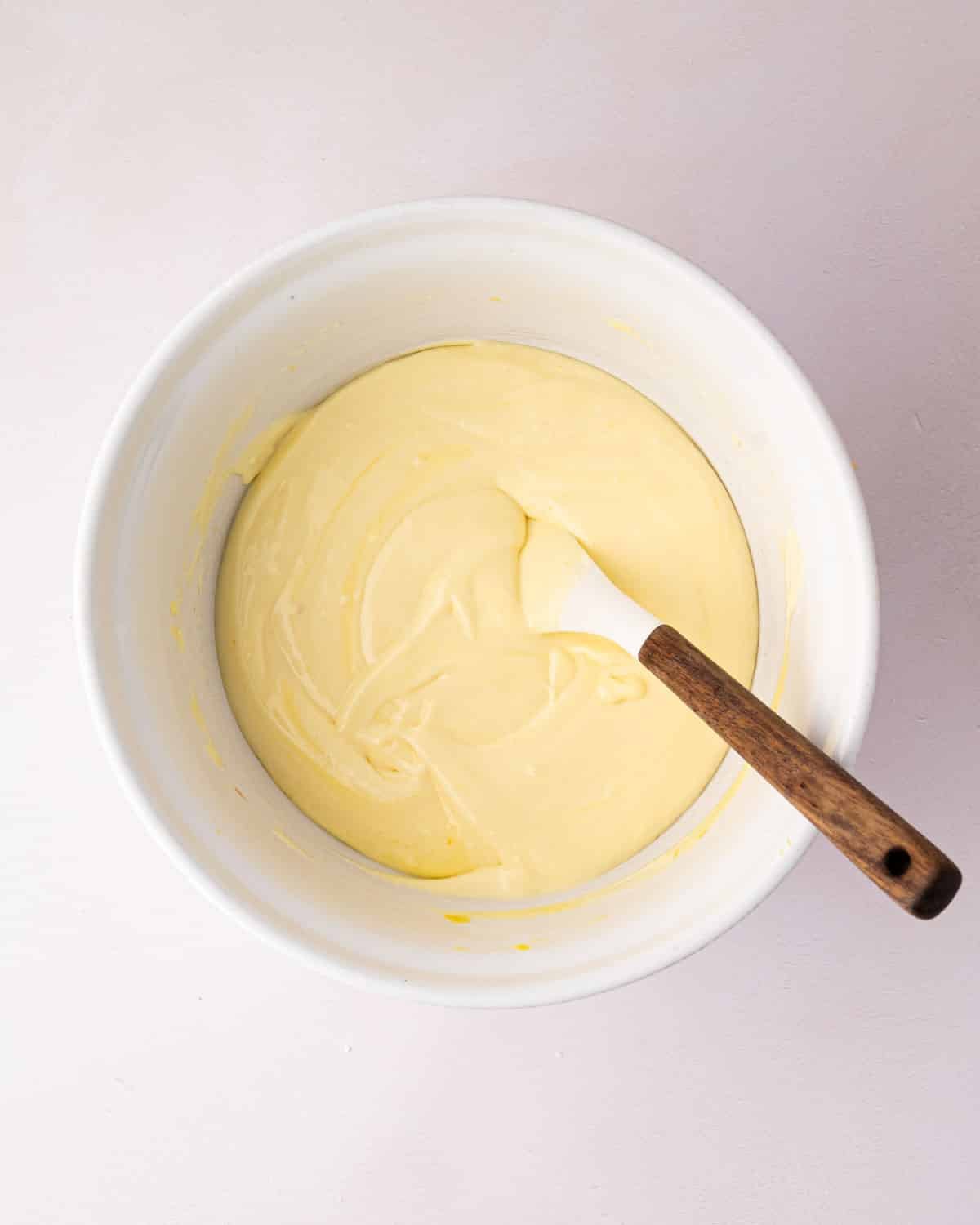 A white bowl with lemon mousse before it's set. A spatula is resting on the side.