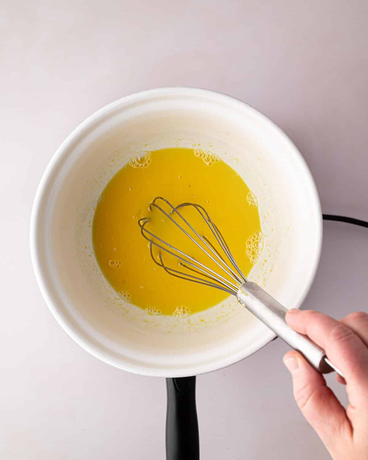 A white bowl with lemon juice and sugar. A hand holding a whisk.