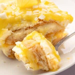 A fork taking a bite out of lemoncello tiramisu with a slice on a white plate.