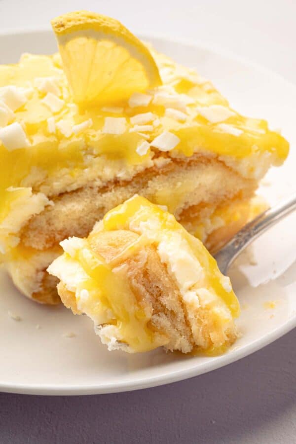 A fork taking a bite out of lemoncello tiramisu with a slice on a white plate.
