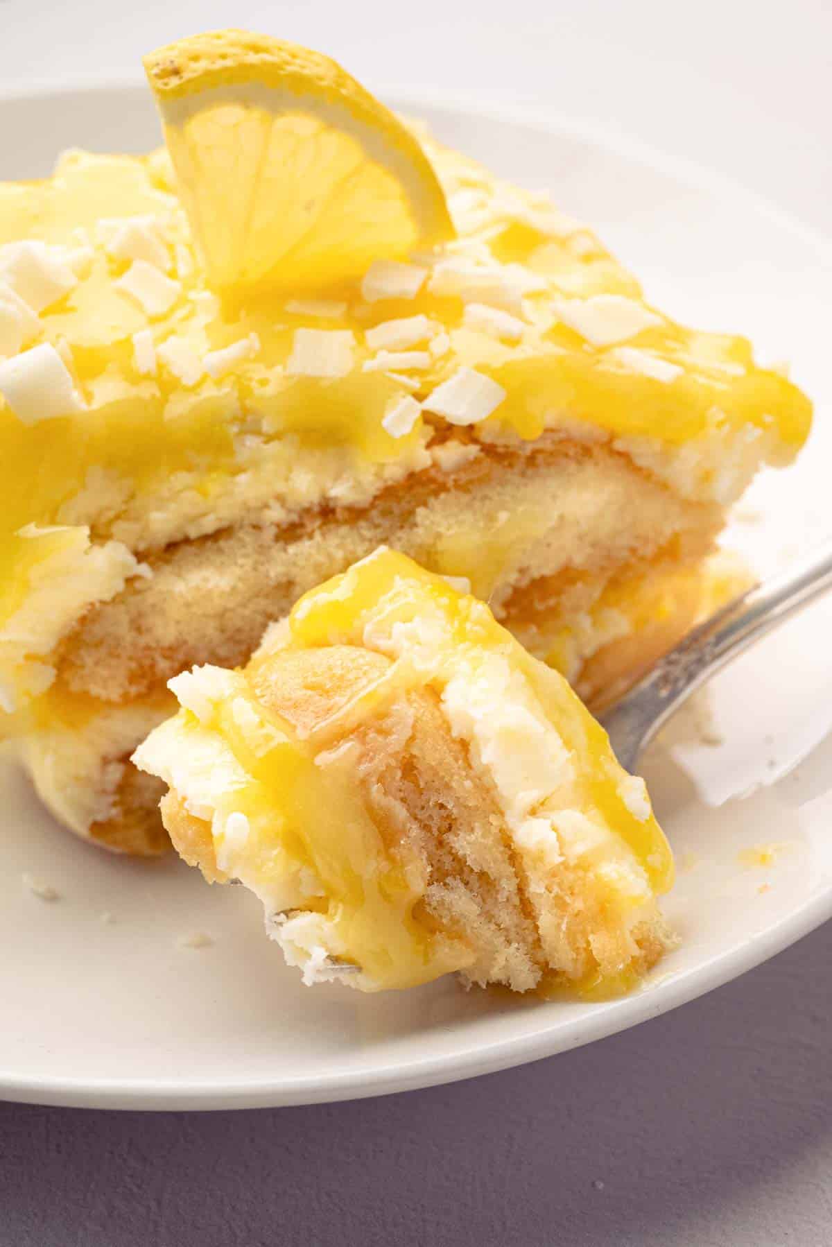 A fork taking a bite out of lemoncello tiramisu with a slice on a white plate.