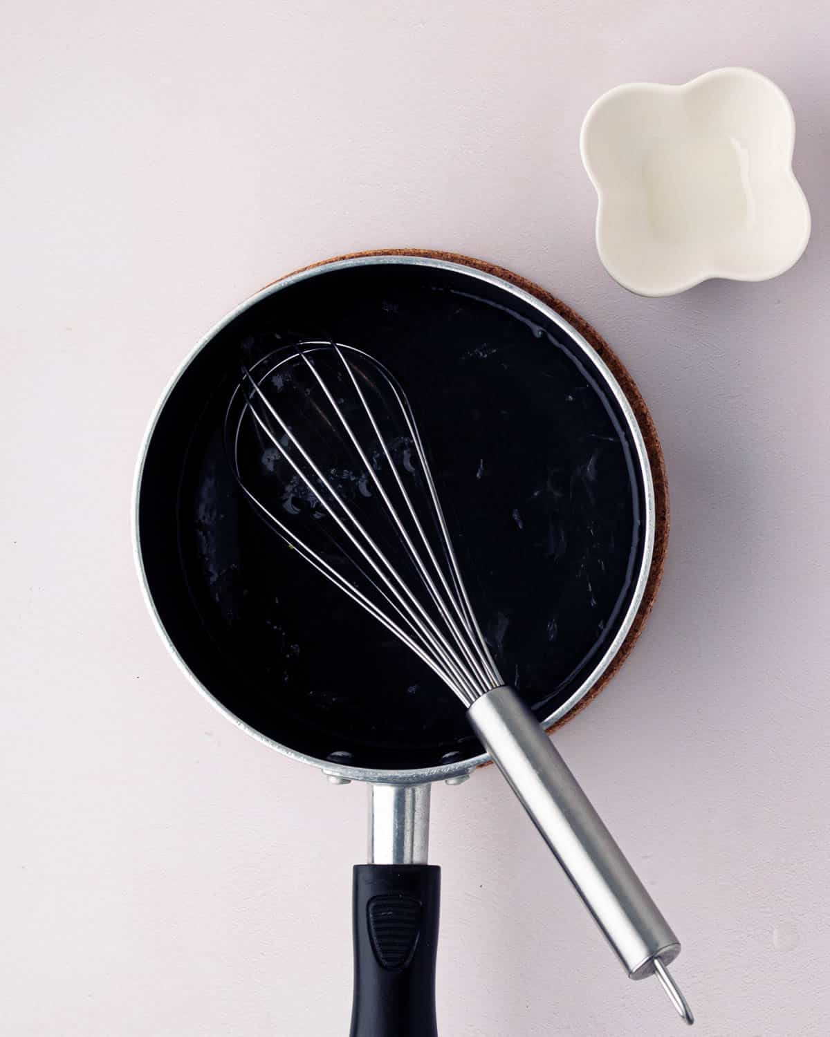 A small black skillet with sugar and water cooking and a whisk resting on the side.